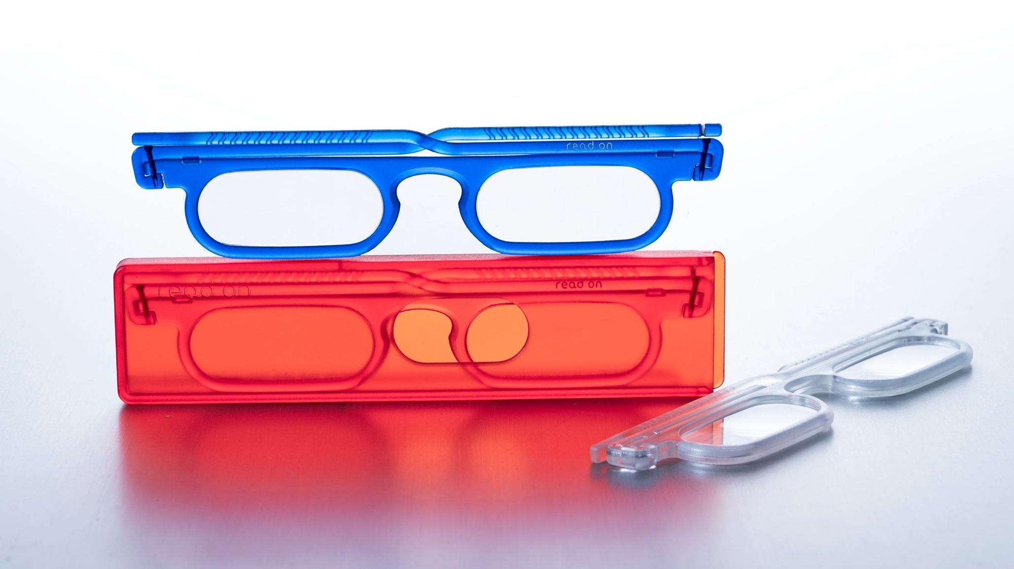 Blue read on bold reading glasses resting on a red case, with transparent crystal frames beside it