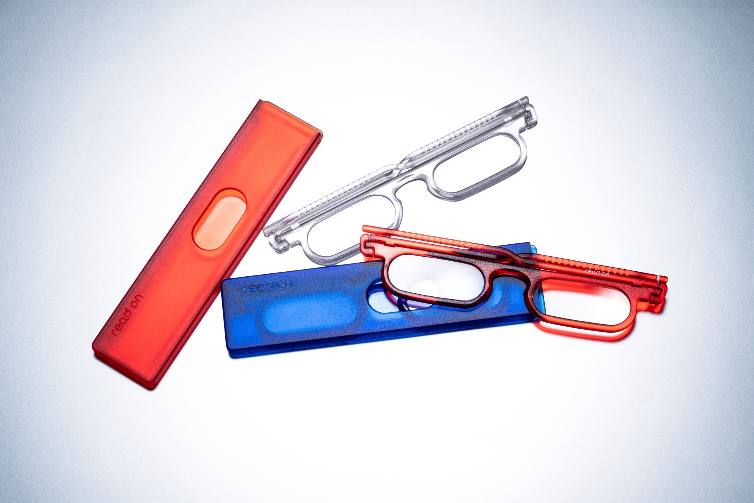 Lunettes de lecture read on bold en rouge transparent, bleu et cristal, présentées avec leurs étuis assortis rouge et bleu