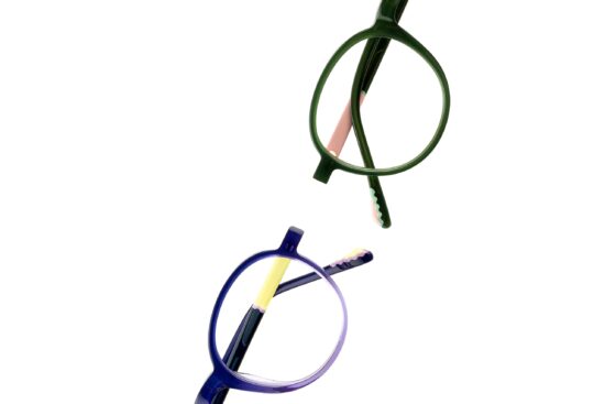 Top-down close-up of two round TREE Spectacles eyewear frames in green and blue, highlighting subtle graphic details and wave accents on the temple tips.