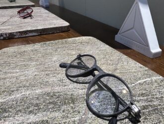 Alt text: Light MONTESTELLA bio-based carbon fiber optical frames displayed on a natural stone exhibit surface.