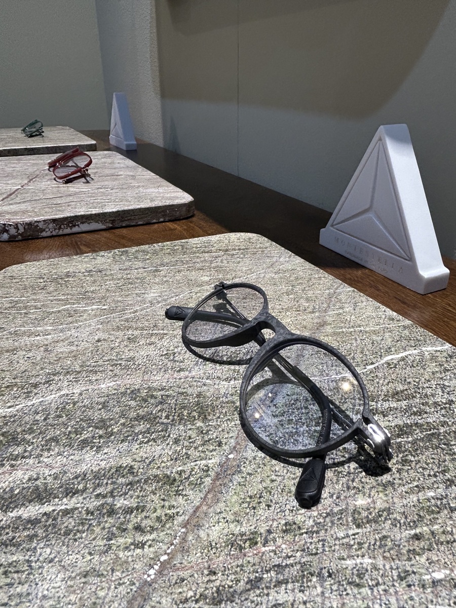 Alt text: Light MONTESTELLA bio-based carbon fiber optical frames displayed on a natural stone exhibit surface.