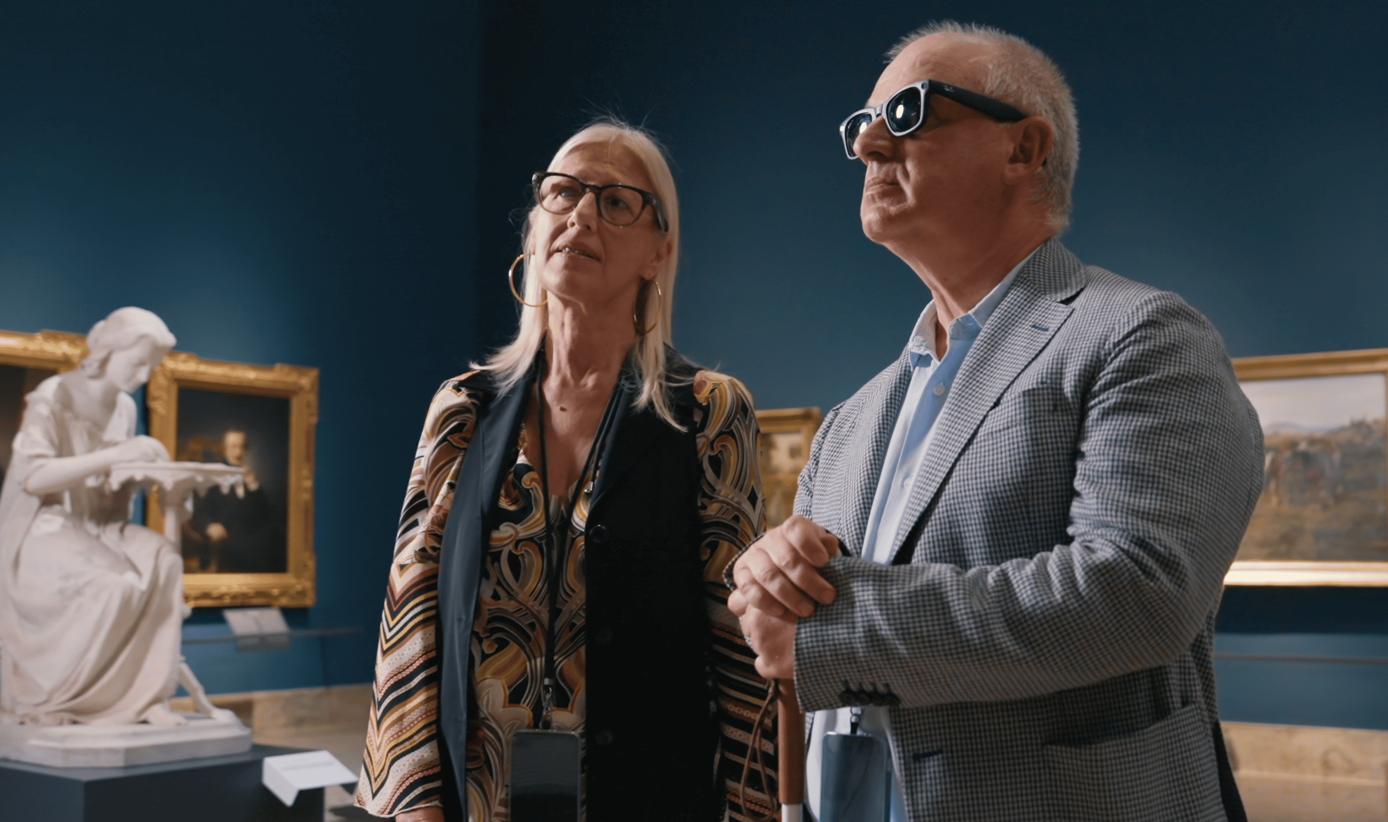 A visually impaired visitor wearing smart glasses and holding a white cane experiences an accessible art exhibition at Pinacoteca di Brera